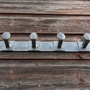 May include: A metal coat rack with six hooks made from large, silver-colored nails. The rack is mounted on a wooden wall.