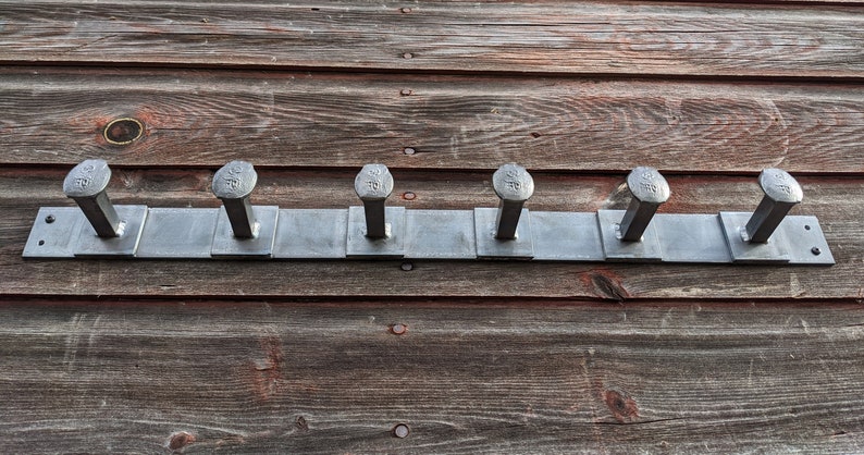 May include: A metal coat rack with six hooks made from large, silver-colored nails. The rack is mounted on a wooden wall.