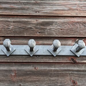 May include: A metal coat rack with six hooks made from large nails mounted on a wooden wall. The hooks are arranged in a row and are all the same size and shape.