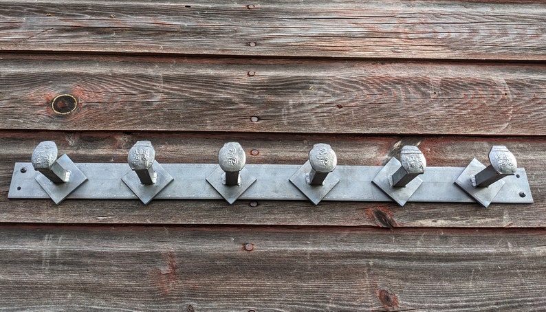 May include: A metal coat rack with six hooks made from large nails mounted on a wooden wall. The hooks are arranged in a row and are all the same size and shape.