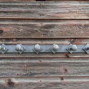 May include: A metal coat rack with six hooks, mounted on a wooden wall. The hooks are made from repurposed metal parts, each with a unique design.