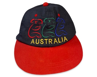 May include: A black and red baseball cap with three colorful embroidered koalas and the word "AUSTRALIA" in yellow lettering.