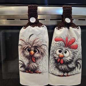May include: Two white kitchen towels with whimsical chicken and owl illustrations. Each towel has a brown crocheted top with a white button for hanging. The chicken has a red comb and the owl has big eyes.