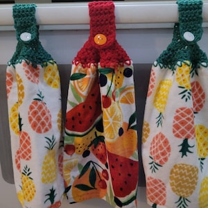 May include: Three kitchen towels with crocheted loops. The towels have a white background with a pineapple pattern. The loops are green, red, and green.