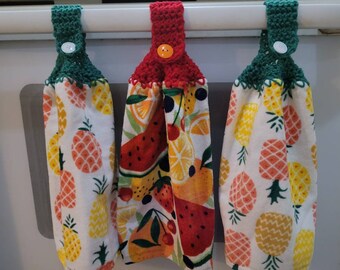 May include: Three kitchen towels with crocheted loops. The towels have a white background with a pineapple pattern. The loops are green, red, and green.