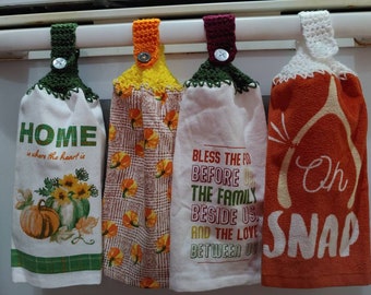 May include: Four kitchen towels with crocheted hangers. The towels have different designs and sayings. One towel says "Home is where the heart is" and has a pumpkin design. Another towel says "Bless the food before us, the family beside us, and the love between us". A third towel has a pumpkin design and the fourth towel says "Oh Snap".