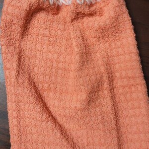May include: A peach-colored kitchen towel with a white crocheted loop and button at the top.
