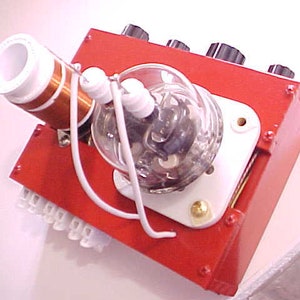 May include: A red electronic device with a white tube, a coil of wire, and several knobs. The device is connected to a white wire.