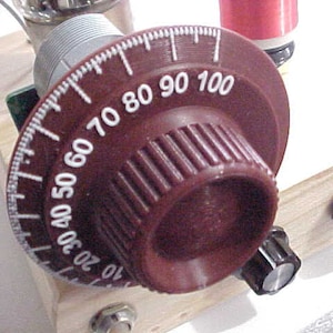 May include: A close-up of a brown rotary dial with white numbers from 10 to 100. The dial is part of an electronic component, with other knobs and components visible.
