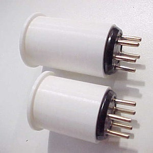May include: Two white ceramic tube sockets with black plastic bases and multiple gold-colored metal pins.