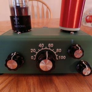 May include: A green vintage radio with a dial marked 0 to 100, four knobs, and a vacuum tube. The radio has a red coil on top and the text "Made in USA National" on the side.