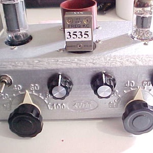 May include: A silver metal box with three knobs and two vacuum tubes. The box has a label that says "KW71" and a frequency counter that reads "3535".
