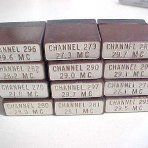 May include: A stack of 12 brown plastic boxes with white labels. Each box has a channel number and frequency printed on it. The channel numbers range from 270 to 297. The frequencies are in MHz.
