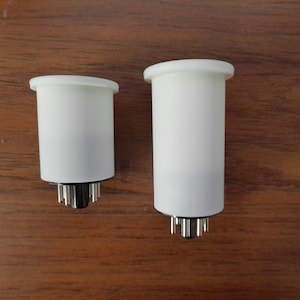 May include: Two white ceramic tube sockets with metal pins. The larger socket is taller than the smaller socket.