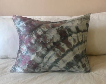 May include: A decorative pillow with a tie-dye pattern in shades of pink, gray, and green. The pillow is made of a soft, silky fabric.