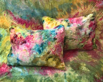 Puede incluir: Dos cojines rectangulares con un vibrante estampado tie-dye en tonos rosa, amarillo, azul y verde. Los cojines descansan sobre una tela tie-dye a juego, creando una exhibición cohesiva y colorida. Los cojines son un acento decorativo para el hogar.