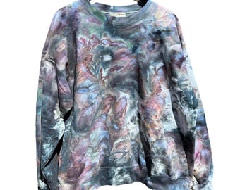 May include: A tie-dye sweatshirt in shades of blue, purple, and gray hangs from a black hanger. The crew neck sweatshirt has long sleeves and a relaxed fit. The fabric has a marbled, watercolor-like pattern. The garment is made of a soft material.
