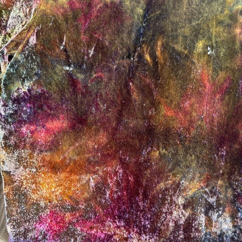 K&ouml;nnte beinhalten: Abstrakter Textilstoff mit einer lebendigen Farbpalette. Der Stoff weist eine Mischung aus tiefen Rott&ouml;nen, Orange und Lila auf, mit Andeutungen von Gold und Gr&uuml;n. Die Textur wirkt weich und m&ouml;glicherweise samtig, was einen reichen, k&uuml;nstlerischen Effekt erzeugt.