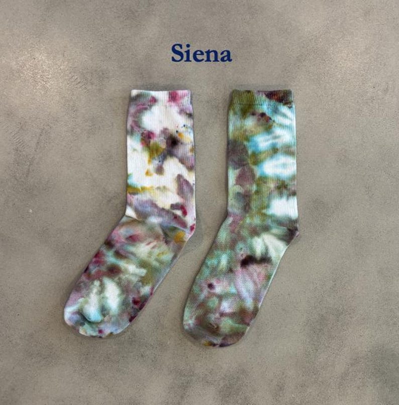 Puede incluir: Un par de calcetines de media ca&ntilde;a con un patr&oacute;n de te&ntilde;ido anudado en tonos blanco, rosa, verde y marr&oacute;n. La palabra "Siena" est&aacute; impresa en azul sobre los calcetines. Los calcetines tienen un pu&ntilde;o acanalado y un aspecto suave y mezclado.
