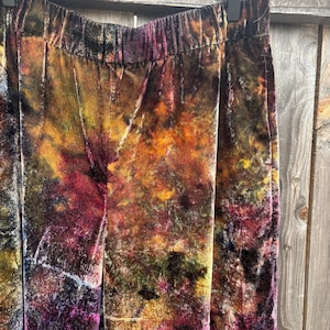 K&ouml;nnte beinhalten: Nahaufnahme einer Samthose mit elastischem Bund. Die Hose hat ein Batikmuster in Braun-, Orange-, Gelb- und Lilat&ouml;nen. Der Stoff hat ein weiches, strukturiertes Aussehen.