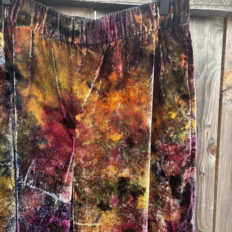 K&ouml;nnte beinhalten: Nahaufnahme einer Samthose mit elastischem Bund. Die Hose hat ein Batikmuster in Braun-, Orange-, Gelb- und Lilat&ouml;nen. Der Stoff hat ein weiches, strukturiertes Aussehen.