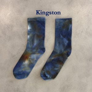 Puede incluir: Un par de calcetines de media ca&ntilde;a con un patr&oacute;n de te&ntilde;ido anudado en tonos azul, marr&oacute;n oscuro y blanco. La palabra Kingston est&aacute; impresa en azul oscuro sobre los calcetines. Los calcetines tienen un pu&ntilde;o acanalado y una textura suave.