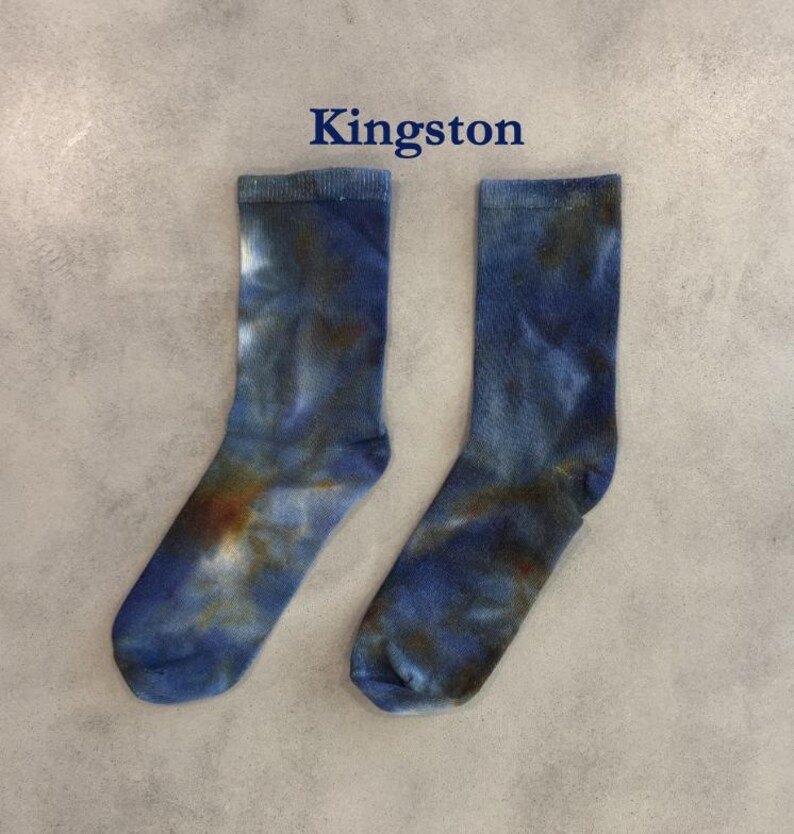 Puede incluir: Un par de calcetines de media ca&ntilde;a con un patr&oacute;n de te&ntilde;ido anudado en tonos azul, marr&oacute;n oscuro y blanco. La palabra Kingston est&aacute; impresa en azul oscuro sobre los calcetines. Los calcetines tienen un pu&ntilde;o acanalado y una textura suave.