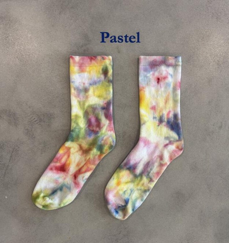 Puede incluir: Un par de calcetines de media ca&ntilde;a con un patr&oacute;n de te&ntilde;ido anudado en varios colores pastel, incluyendo amarillo, rosa, azul y verde. La palabra Pastel est&aacute; impresa en azul oscuro sobre los calcetines, que tienen un pu&ntilde;o acanalado y textura.
