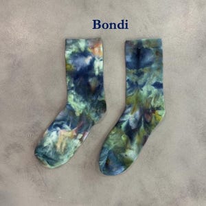 Puede incluir: Un par de calcetines de media ca&ntilde;a con un patr&oacute;n de te&ntilde;ido anudado en tonos azul oscuro, verde bosque y toques de amarillo. La palabra Bondi est&aacute; impresa en azul oscuro sobre los calcetines, que tienen una textura acanalada en el tejido.