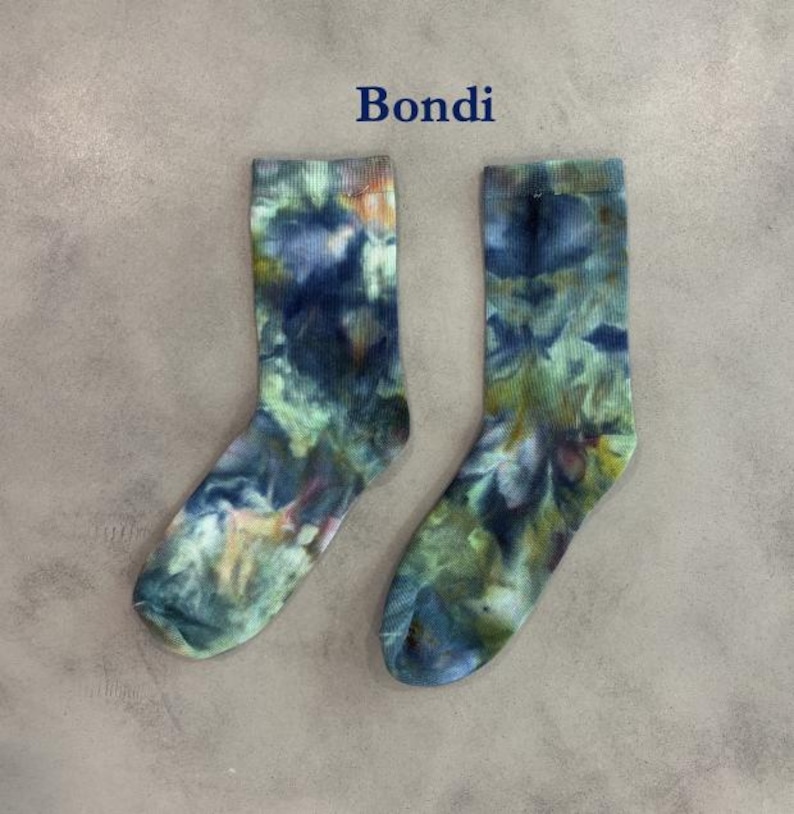 Puede incluir: Un par de calcetines de media ca&ntilde;a con un patr&oacute;n de te&ntilde;ido anudado en tonos azul oscuro, verde bosque y toques de amarillo. La palabra Bondi est&aacute; impresa en azul oscuro sobre los calcetines, que tienen una textura acanalada en el tejido.