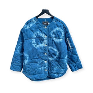 May include: A blue quilted jacket with a white tie-dye pattern. The jacket has a button closure and a zippered pocket on the sleeve. The label on the jacket reads "Urban Outfitters".