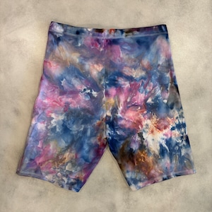 May include: Tie-dye bike shorts in shades of blue, pink, and brown. The shorts have a high waist and a relaxed fit.