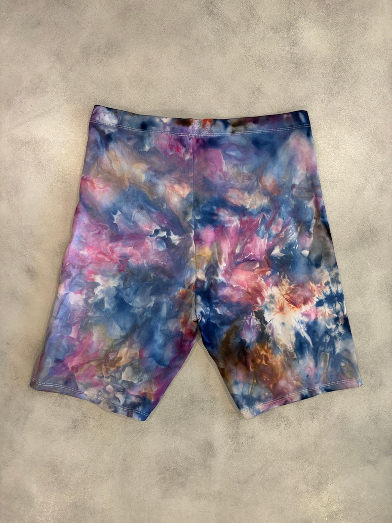 May include: Tie-dye bike shorts in shades of blue, pink, and brown. The shorts have a high waist and a relaxed fit.