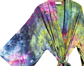May include: A tie-dye kimono robe featuring a vibrant blend of blue, green, yellow, and pink colors. The garment has wide, loose sleeves, a wrap-front design with a matching fabric tie belt, and a label at the neckline that reads TACANA.