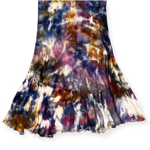 Pode incluir: Uma saia tie-dye em tons de azul, roxo, castanho e branco. A saia tem uma silhueta rodada, com as cores misturando-se num padr&atilde;o &uacute;nico. O tecido parece macio e fluido.