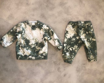 May include: A green and white tie-dye sweatshirt and matching sweatpants. The sweatshirt has a crew neck and long sleeves. The sweatpants have an elastic waistband and a drawstring.