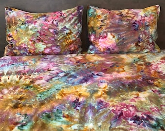 May include: A bed with a brown headboard and a colorful tie-dye duvet cover and pillowcases. The duvet cover and pillowcases have a swirling pattern of pink, purple, green, and yellow.