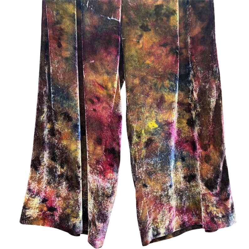 K&ouml;nnte beinhalten: Breite Samthose mit einem lebendigen Batikmuster in Braun-, Lila-, Gelb- und Rosat&ouml;nen. Die Hose hat eine vertikale Naht auf der Vorderseite jedes Beins, wodurch eine flie&szlig;ende Silhouette entsteht.