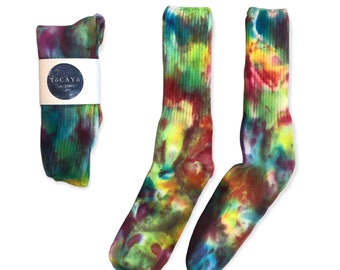May include: A pair of colorful tie-dye socks with a green, yellow, red, and blue pattern. The socks are folded and displayed on a white background. The socks have a ribbed texture and are made of cotton.