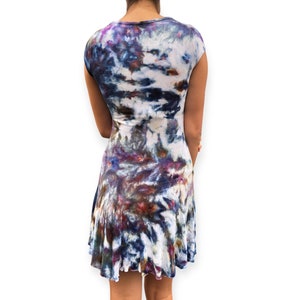 Pode incluir: Vestido tie-dye com decote redondo e mangas curtas. O vestido tem uma saia rodada e um padr&atilde;o de tons brancos, azuis, roxos e castanhos. O tecido parece macio e fluido, adequado para roupas casuais.