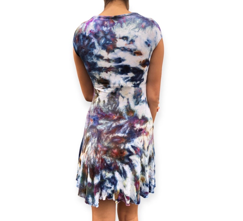 Pode incluir: Vestido tie-dye com decote redondo e mangas curtas. O vestido tem uma saia rodada e um padr&atilde;o de tons brancos, azuis, roxos e castanhos. O tecido parece macio e fluido, adequado para roupas casuais.