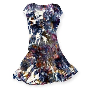 Pode incluir: Vestido tie-dye em tons de azul, branco, roxo e laranja. O vestido tem decote redondo, mangas curtas e saia rodada. Possui abotoamento frontal e uma pequena etiqueta perto da gola.