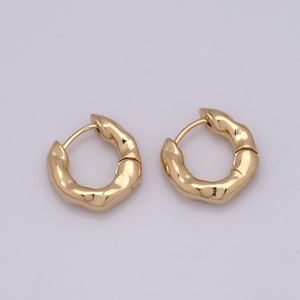 May include: A pair of gold-toned hoop earrings with a textured, irregular surface. The earrings are made of metal and have a hinged closure.