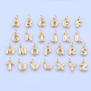 May include: A collection of gold-colored alphabet charms, each with a loop for attaching to a necklace or bracelet. The letters A through Z are displayed, showcasing a variety of fonts and styles. These charms are ideal for personalized jewelry.