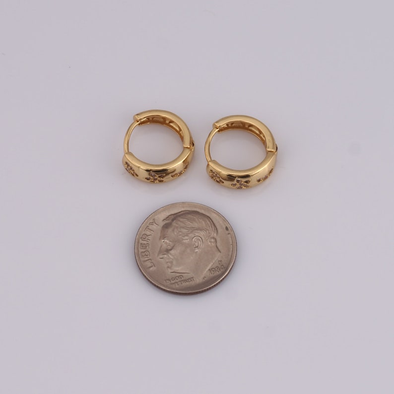 Puede incluir: Un par de pendientes de aro de oro con un peque&ntilde;o dise&ntilde;o brillante alrededor del borde. Los pendientes son aproximadamente del tama&ntilde;o de una moneda de diez c&eacute;ntimos.