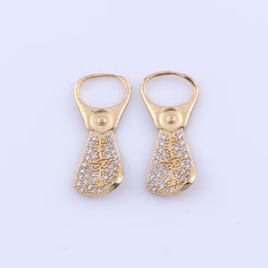 May include: A pair of gold earrings shaped like a can tab with a clear crystal design.