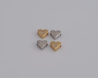 May include: Four heart-shaped beads, two gold and two silver, each encrusted with small, sparkling crystals. The beads are arranged in a square formation against a plain, light background. These beads are ideal for jewelry making.
