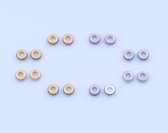 May include: An assortment of small, round jewelry beads. The beads are gold and silver-toned, with colorful gemstones in red, green, blue, and clear. The beads are arranged on a light blue surface.
