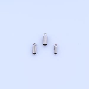 May include: Three small, silver-colored metal tube-shaped jewelry findings with a loop at the top. The findings are of varying sizes, with a cylindrical shape and a polished finish. They are set against a plain white background.