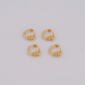 May include: Four gold-colored hoop earrings. Each earring features a snake design with a small red accent. The earrings are arranged on a white surface. The snake's head forms the clasp of the hoop.